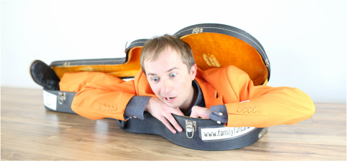 Ryan, Family Fun Band creator, is comically crammed into a guitar case and making a funny face.